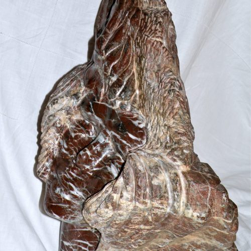 Lucie, ou Lucy l'australopithèque et son univers immortalisée par l'artiste. Le visage de Lucie est tourné vers le ciel. En haut à gauche, est sculpté un soleil, sur le coté droit une ammonite et un coquillage, au verso des feuillages, un oiseau un poisson etune goute d'eau. Ce sont les éléments de surie de Lucie