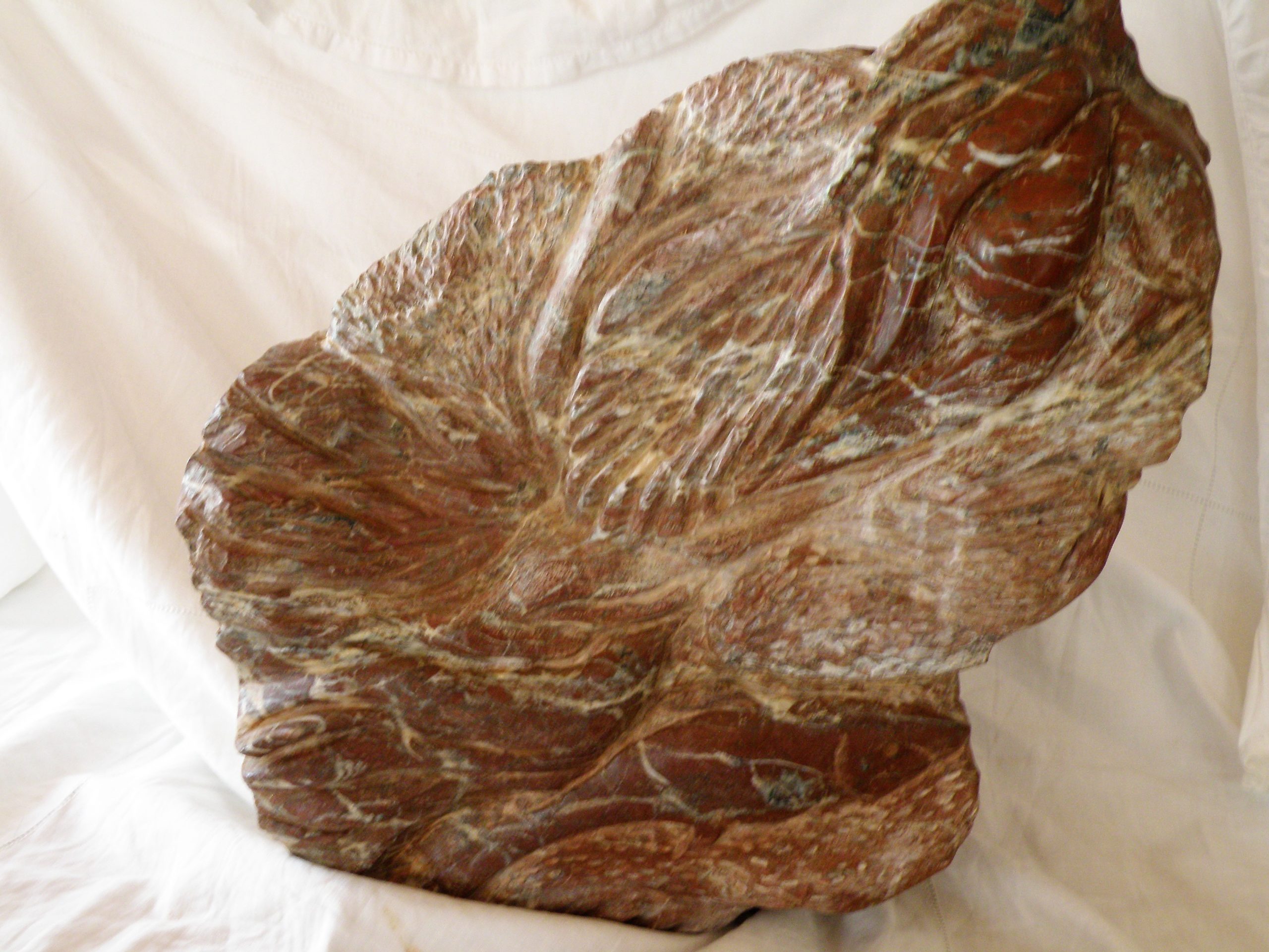 Lucie, ou Lucy l'australopithèque et son univers immortalisée par l'artiste. Le visage de Lucie est tourné vers le ciel. En haut à gauche, est sculpté un soleil, sur le coté droit une ammonite et un coquillage, au verso des feuillages, un oiseau un poisson etune goute d'eau. Ce sont les éléments de surie de Lucie